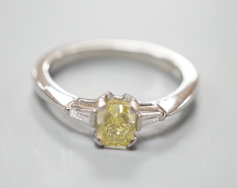A modern platinum and single stone fancy yellow diamond set ring, with trapeze cut diamond set shoulders, size N, gross weight 4.6 grams